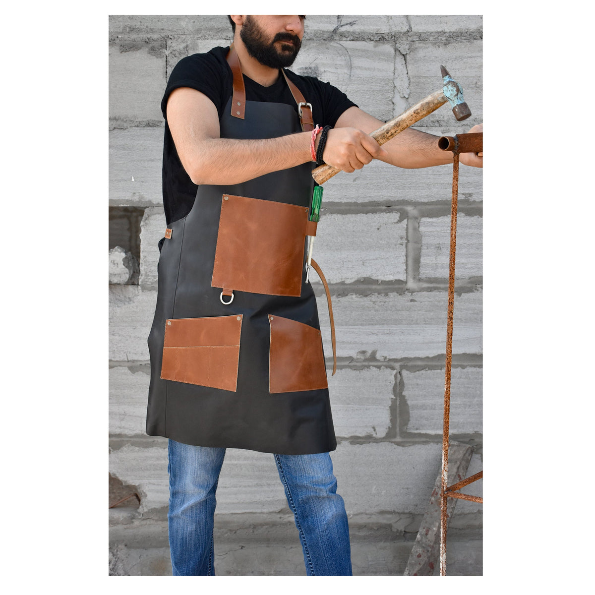 May include: A black leather apron with brown leather pockets and straps. The apron is being worn by a person who is using a hammer to work on a metal structure.