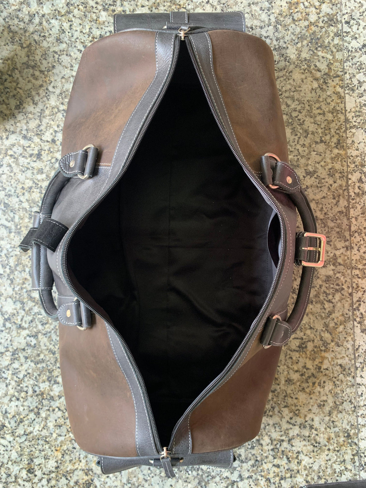 May include: A brown leather duffel bag with black accents and a zipper closure. The bag is open and the inside is lined with black fabric.