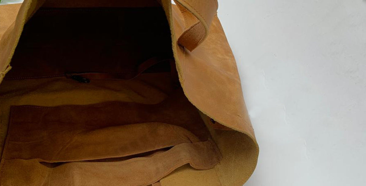 May include: The inside of a brown leather tote bag with a suede pocket. The bag has a single strap and is open at the top.