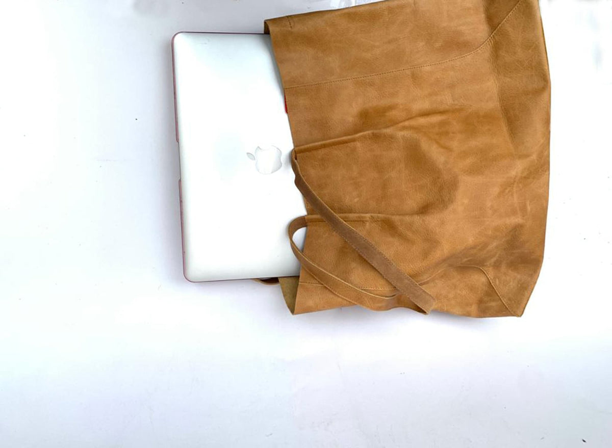 May include: A tan tote bag with a laptop inside. The bag is made of a textured material and has a shoulder strap. The laptop is silver with an Apple logo.