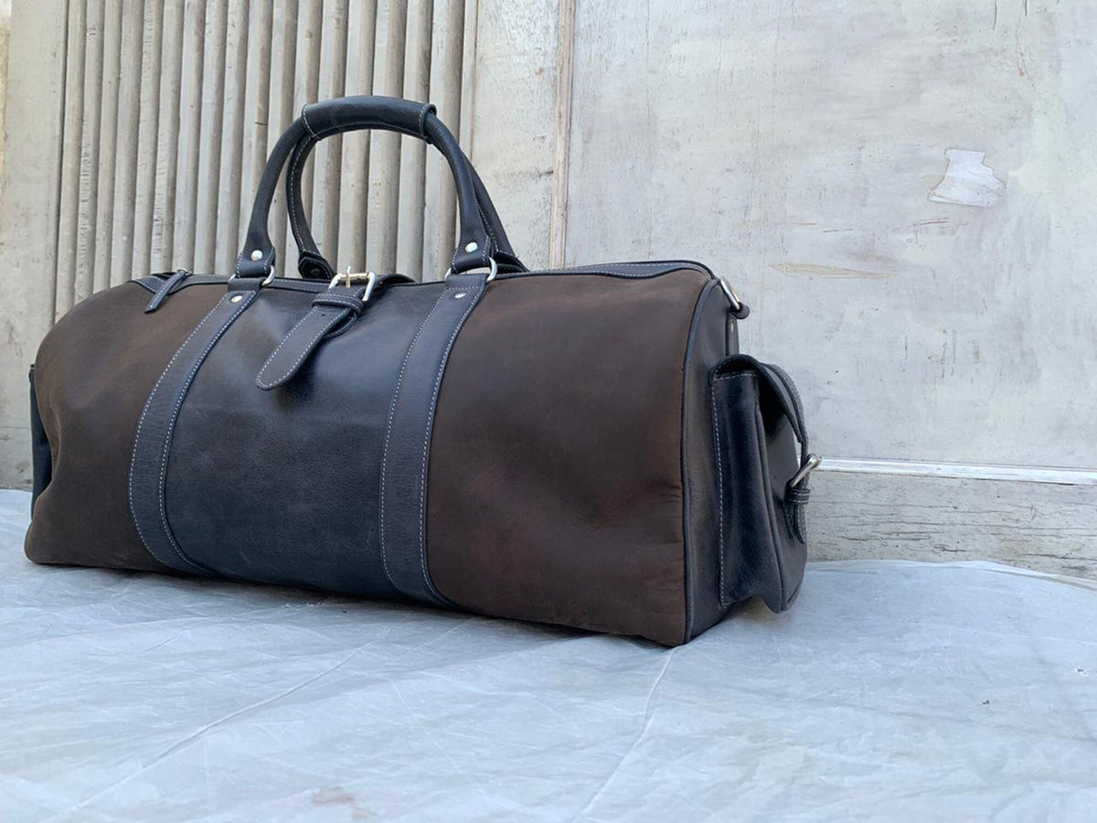 May include: A brown and black leather duffel bag with a top handle and a shoulder strap.