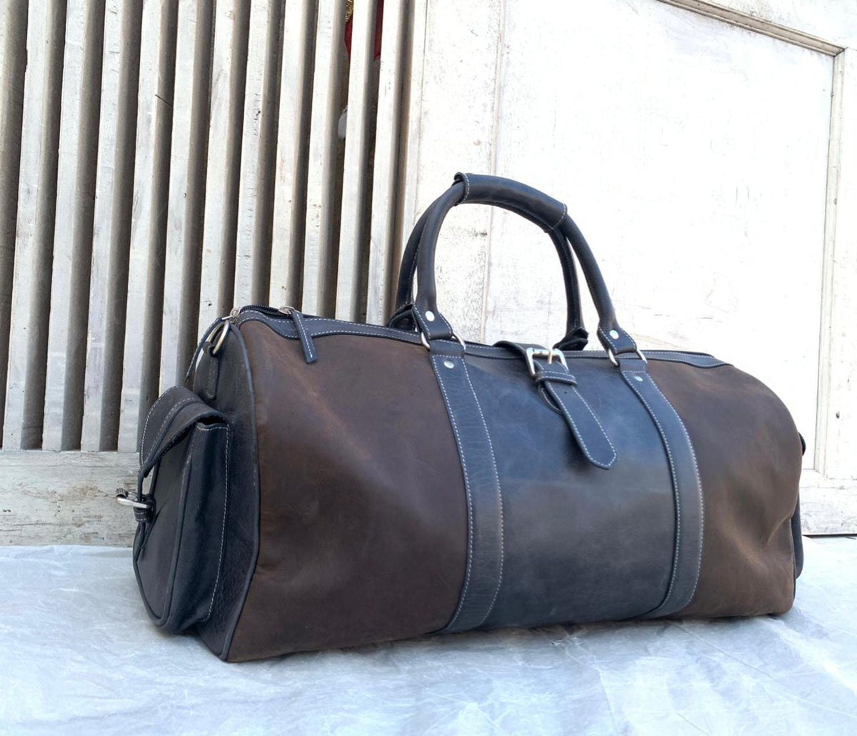 May include: A brown and black leather duffel bag with a top handle and a zippered closure.