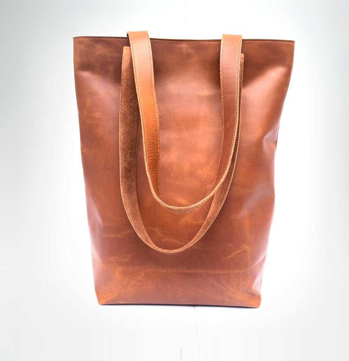 May include: A brown leather tote bag with two long straps. The bag has a slightly distressed look.