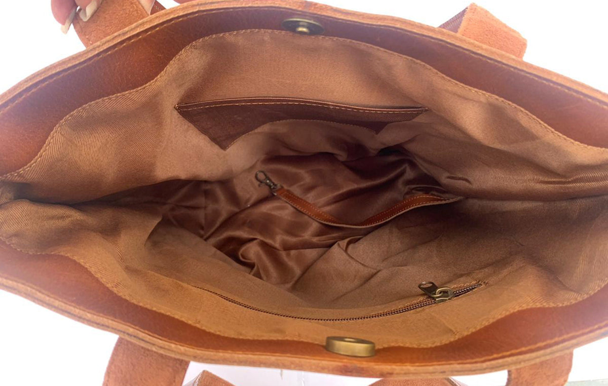 May include: The inside of a brown leather tote bag with a zippered pocket and a small interior pocket. The bag has a brown fabric lining.