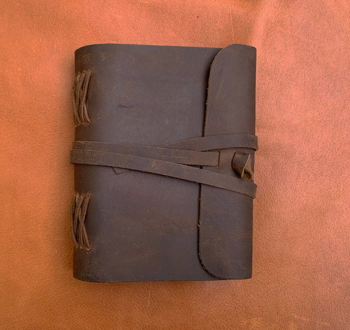May include: A brown leather journal with a flap closure and a braided leather strap. The journal has a rustic, vintage look.