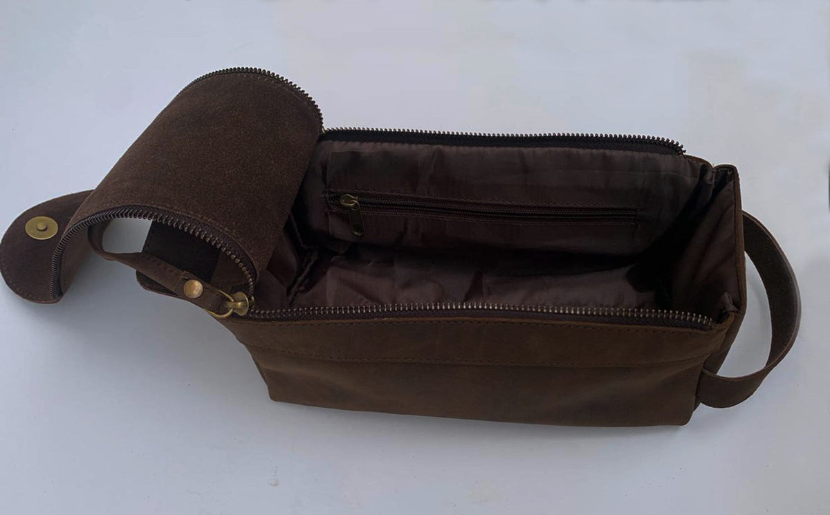 May include: A brown leather travel toiletry bag with a zipper closure and a small interior pocket. The bag has a flap that folds over the top and a handle on each side.