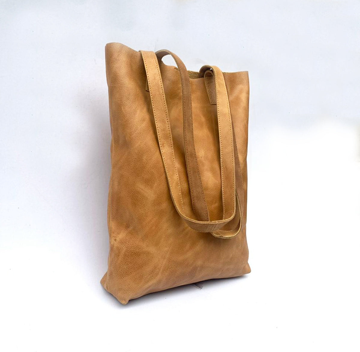 May include: A tan leather tote bag with two long straps. The bag is made of a soft, supple leather and has a casual, relaxed look.