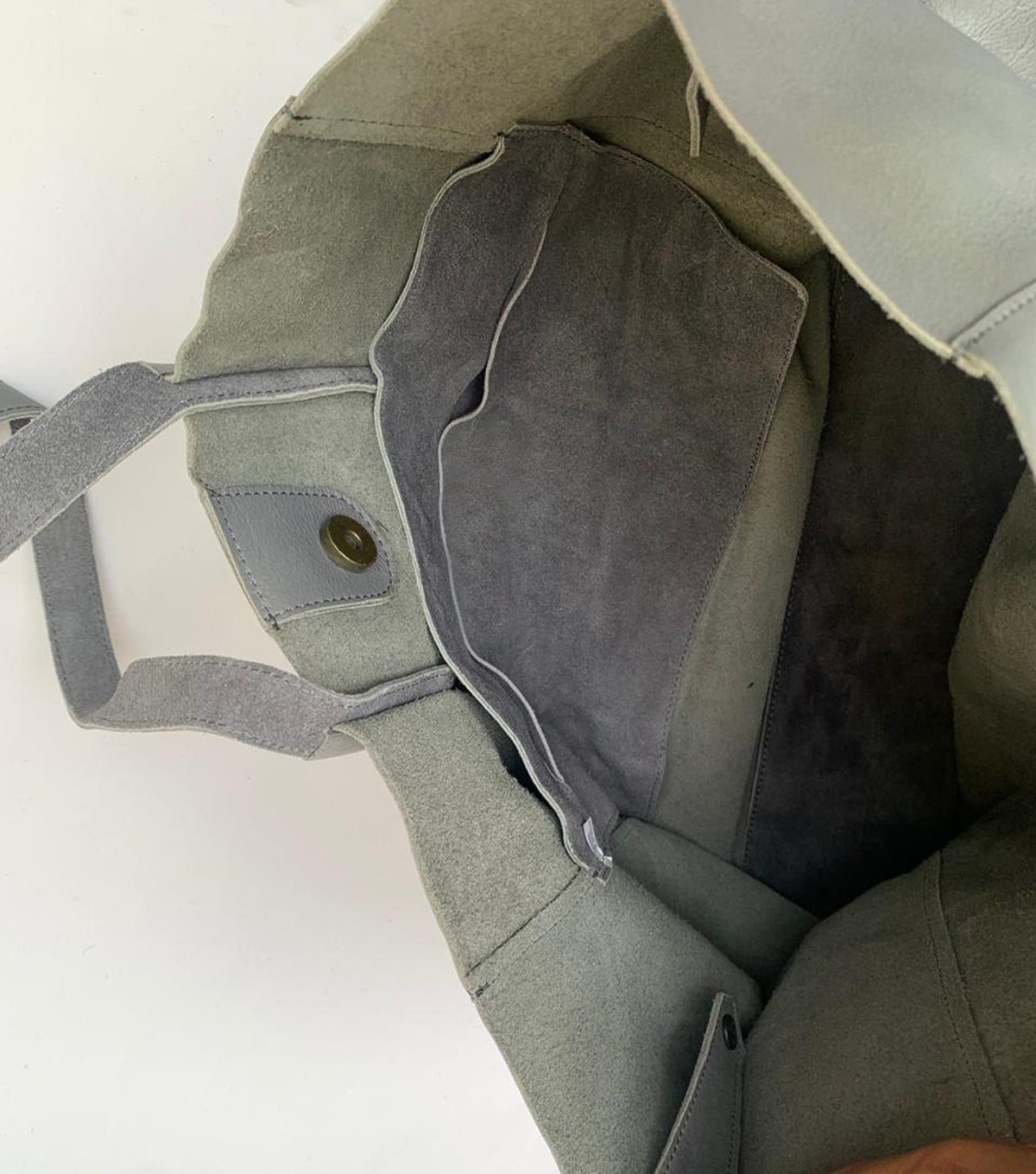 May include: A gray leather tote bag with a large interior pocket and a magnetic snap closure. The bag has two handles and is made of soft, supple leather. The interior is a darker shade of gray.