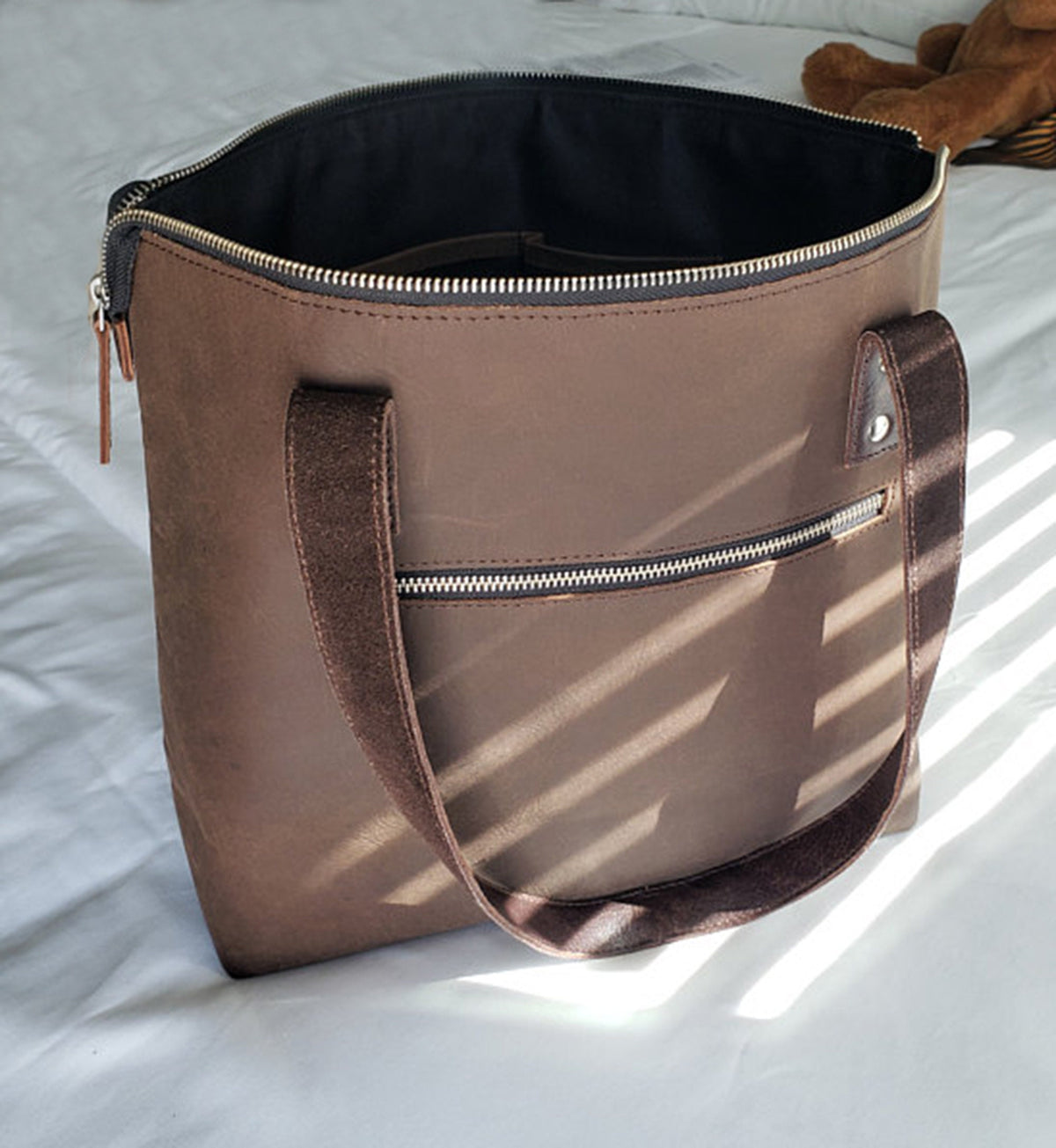 May include: A brown leather tote bag with a zipper closure and two top handles. The bag has a front pocket with a zipper closure.