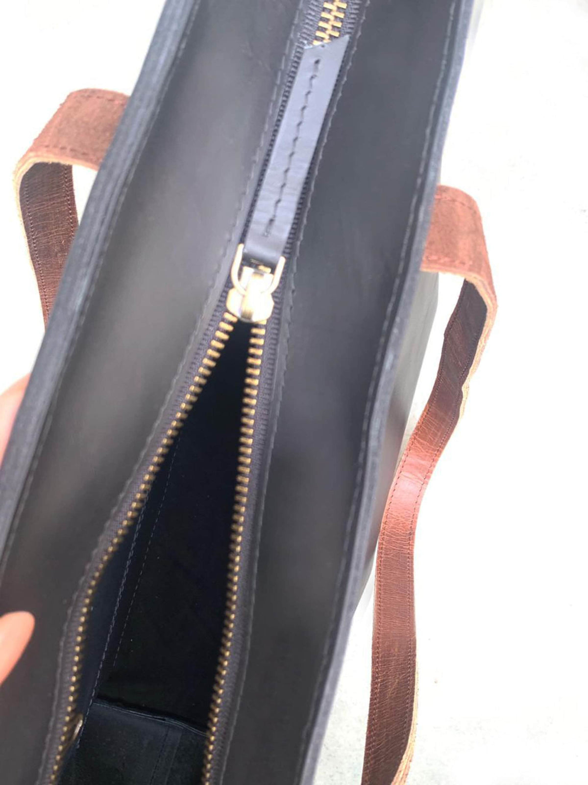 May include: Black leather tote bag with a gold zipper and brown leather handles. The bag is open, revealing the interior. The zipper is partially open, showing the inside of the bag.