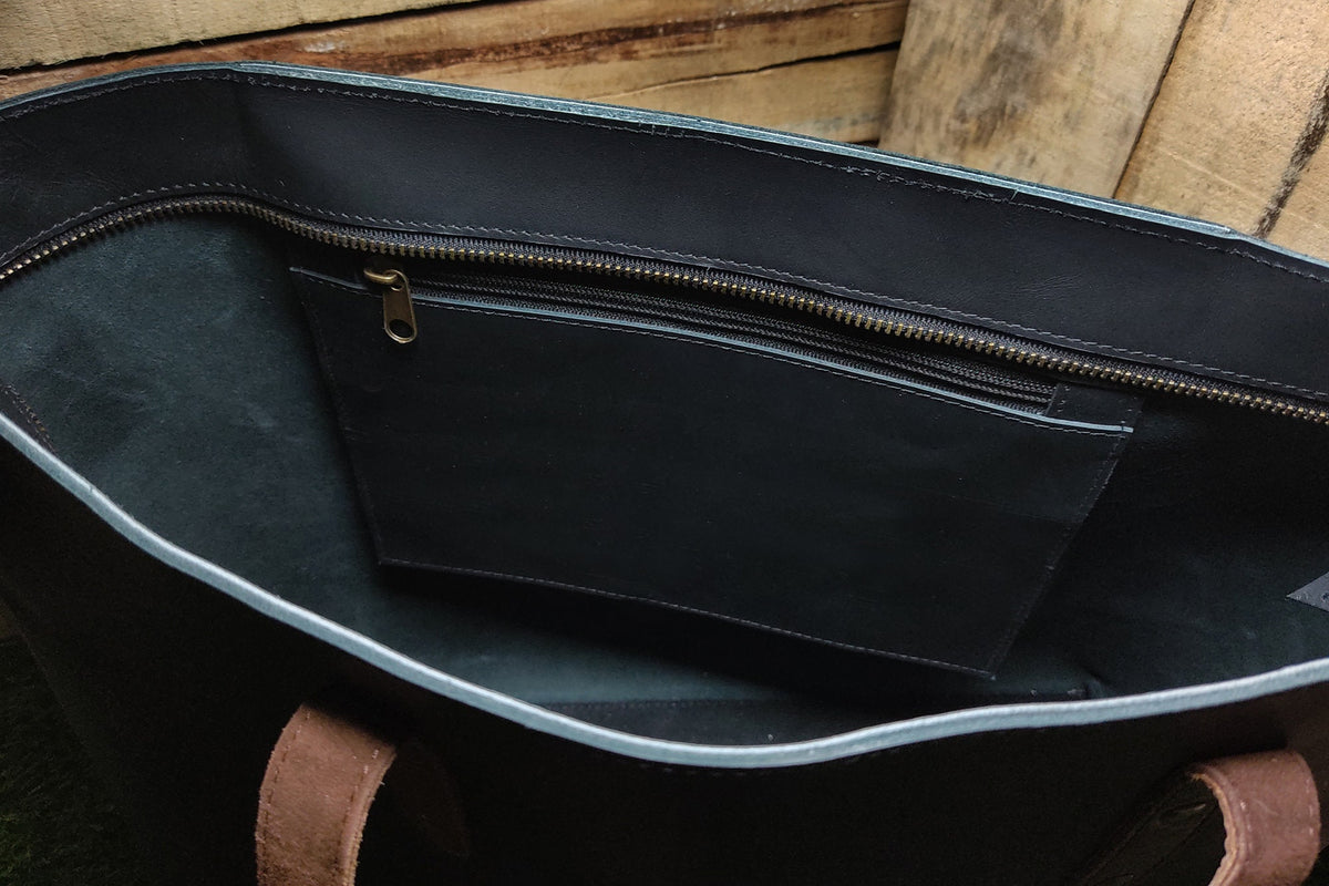 May include: The inside of a black leather tote bag with a zippered pocket. The bag has brown leather handles.