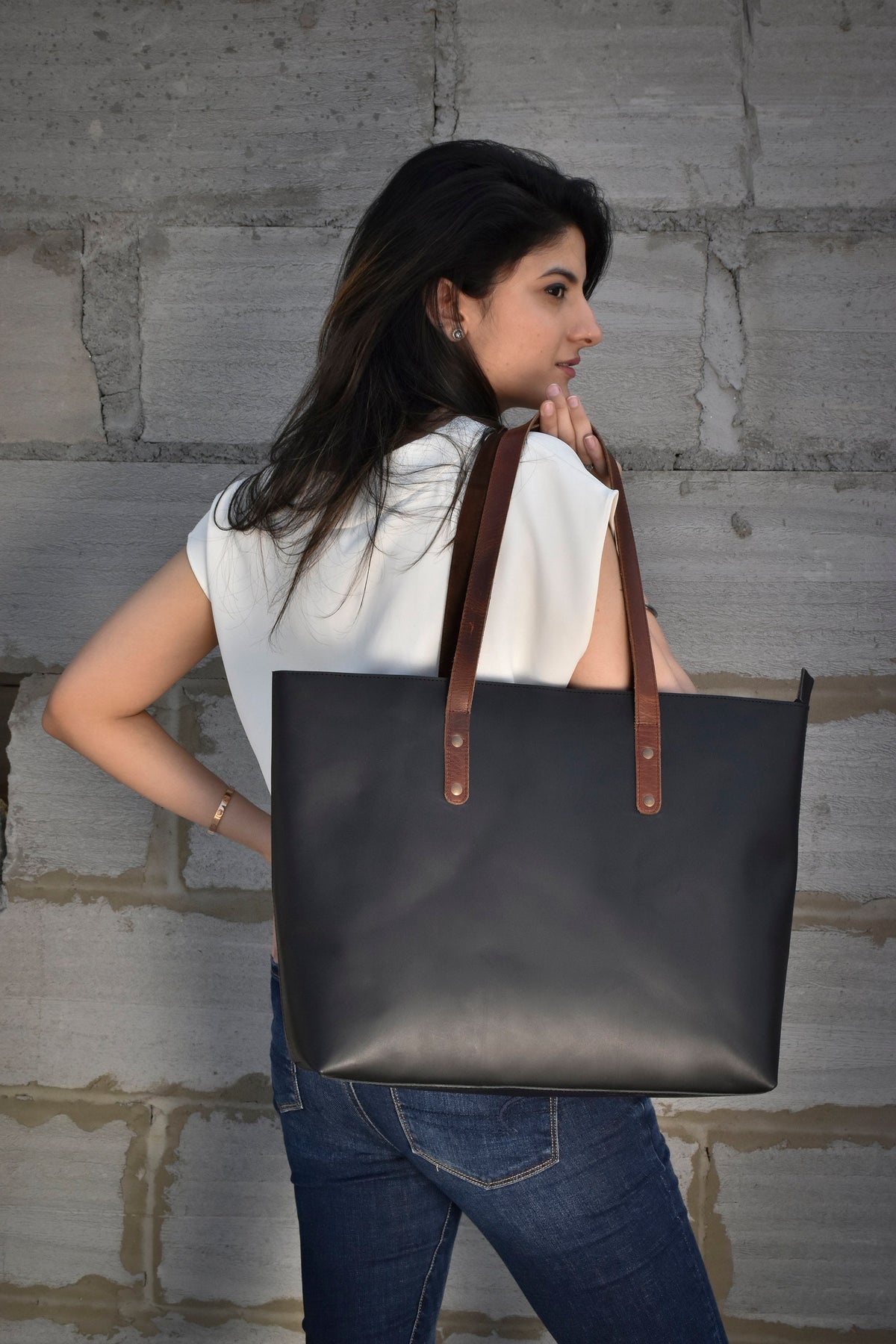 May include: A black leather tote bag with brown leather straps and handles. The bag has a simple design and is large enough to carry everyday essentials.