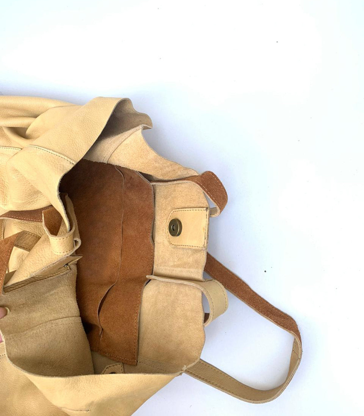 May include: A beige leather tote bag with a brown suede interior. The bag has a magnetic snap closure and a long strap. The bag is open, revealing the interior pockets and construction.