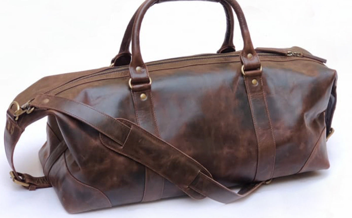 May include: A brown leather duffel bag with a top handle and a shoulder strap. The bag has a zipper closure and brass hardware.