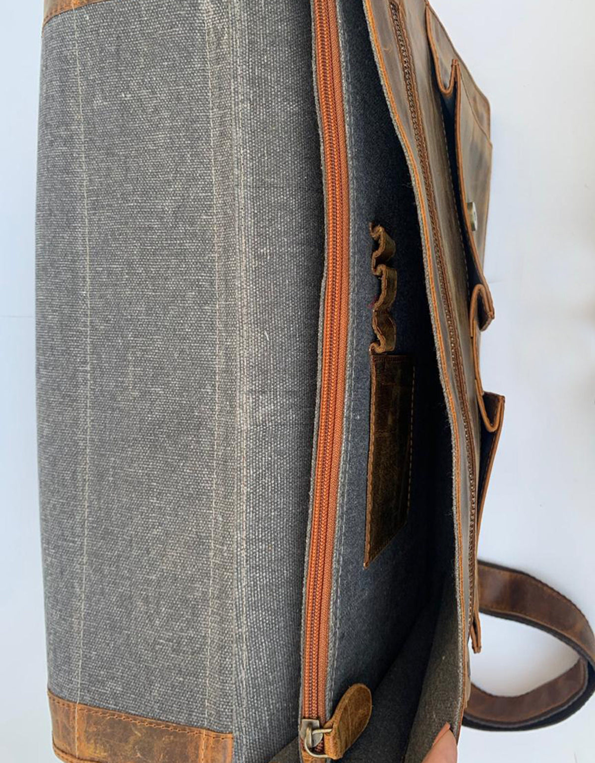 May include: A brown leather messenger bag with a gray canvas lining. The bag has a zipper closure and a small pocket on the front.