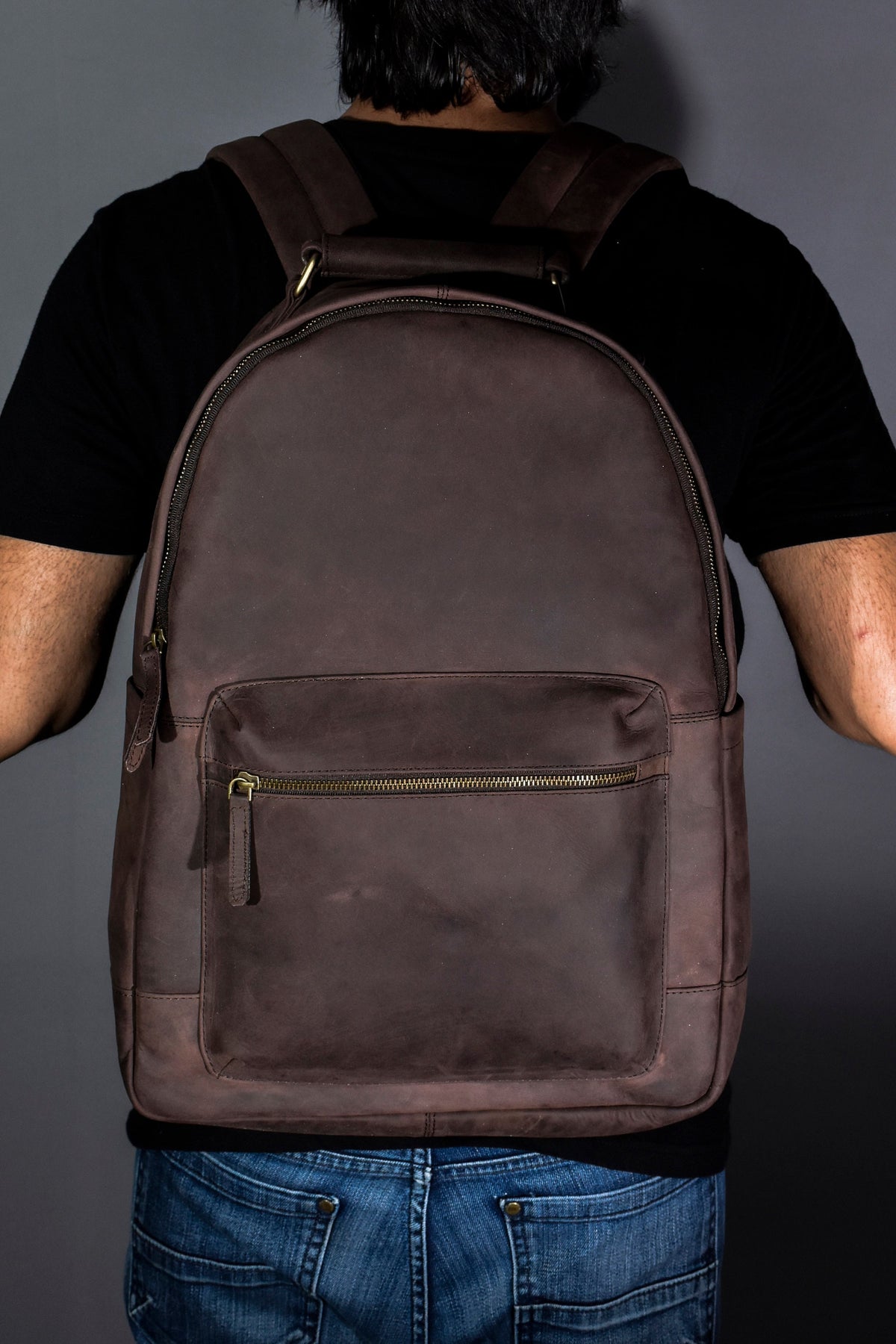 May include: A brown leather backpack with a zippered front pocket. The backpack has a top handle and adjustable straps.
