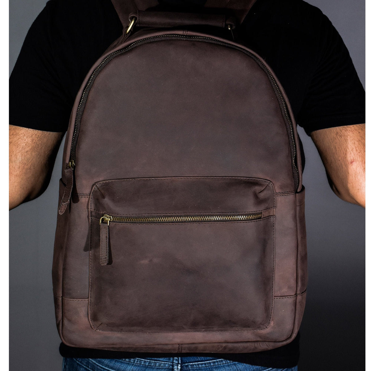 May include: A brown leather backpack with a zippered front pocket. The backpack has a top handle and adjustable straps.