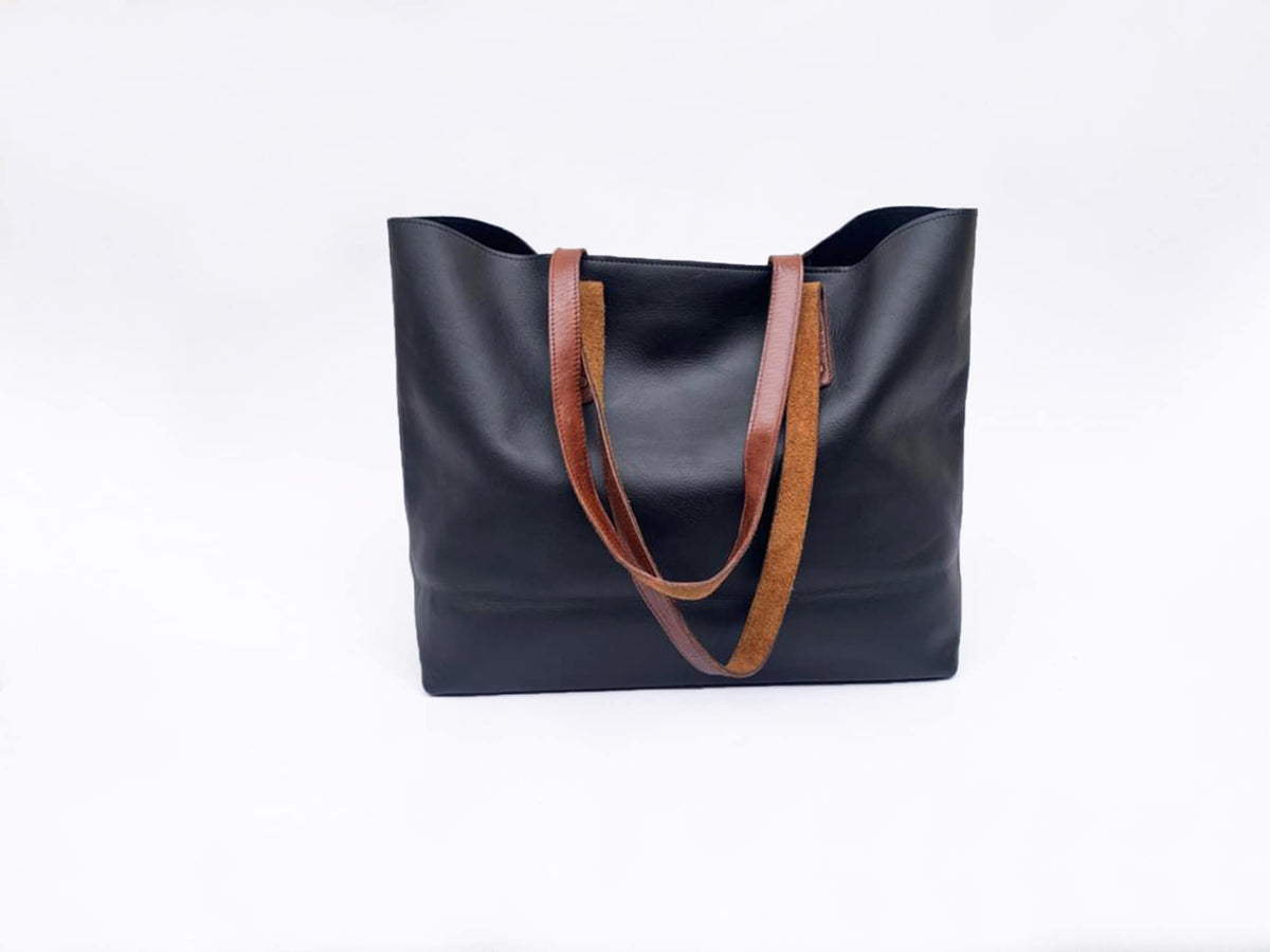 May include: A black tote bag with brown leather straps. The bag is made of a smooth, matte material and has a rectangular shape. The straps are a contrasting color and texture, adding a stylish detail to the design.