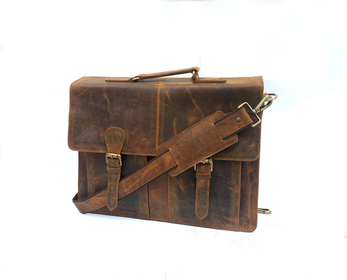 May include: A brown leather briefcase with a top handle and adjustable shoulder strap. The bag features two front buckles and a flap closure. The leather has a distressed appearance with visible grain and texture, and the hardware is gold-toned.
