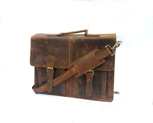 May include: A brown leather briefcase with a top handle and adjustable shoulder strap. The bag features two front buckles and a flap closure. The leather has a distressed appearance with visible grain and texture, and the hardware is gold-toned.