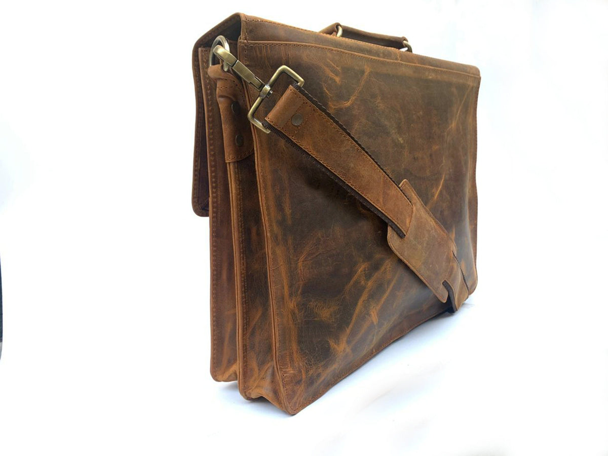May include: A brown leather briefcase with a shoulder strap and a top handle. The bag has a flap closure and brass-colored hardware. The leather has a distressed appearance, with variations in color and texture.