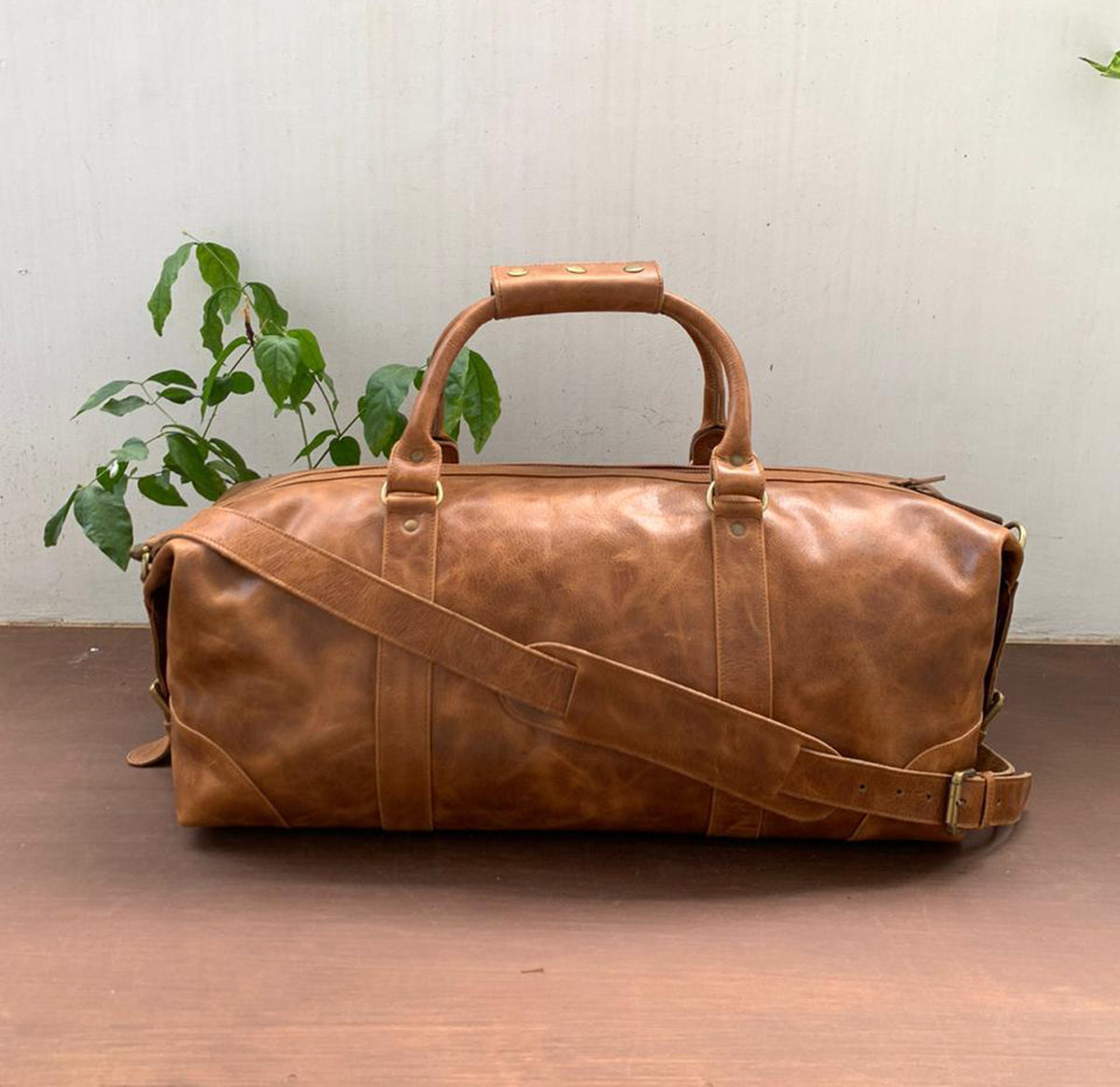 May include: A brown leather duffel bag with a top handle and a shoulder strap. The bag has a distressed look and is made of high-quality leather.