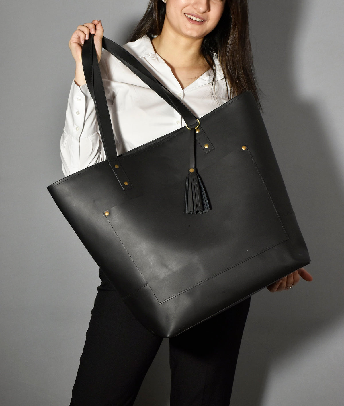May include: A black leather tote bag with a gold tassel and a front pocket. The bag has a top zipper closure and two handles.