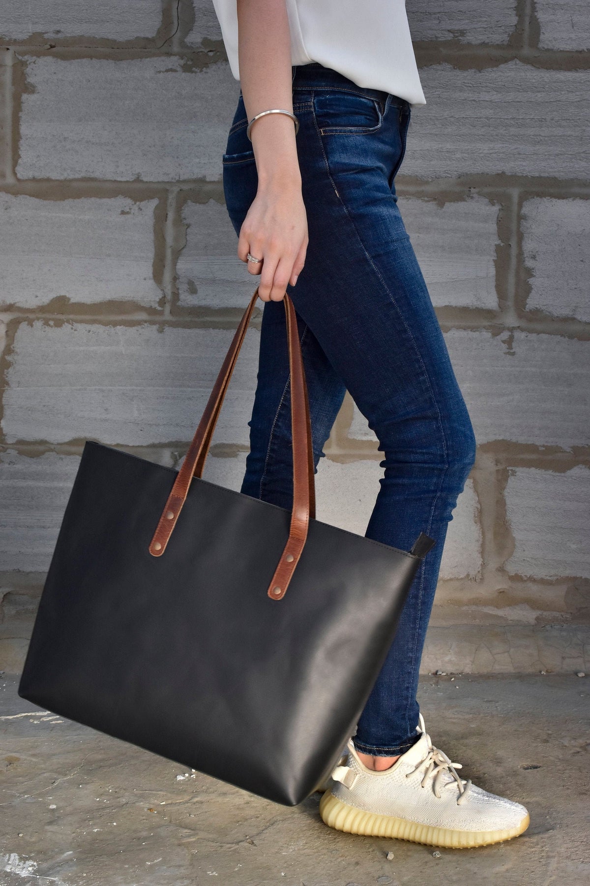 May include: A black leather tote bag with brown leather straps and handles. The bag has a simple design and is large enough to carry everyday essentials.