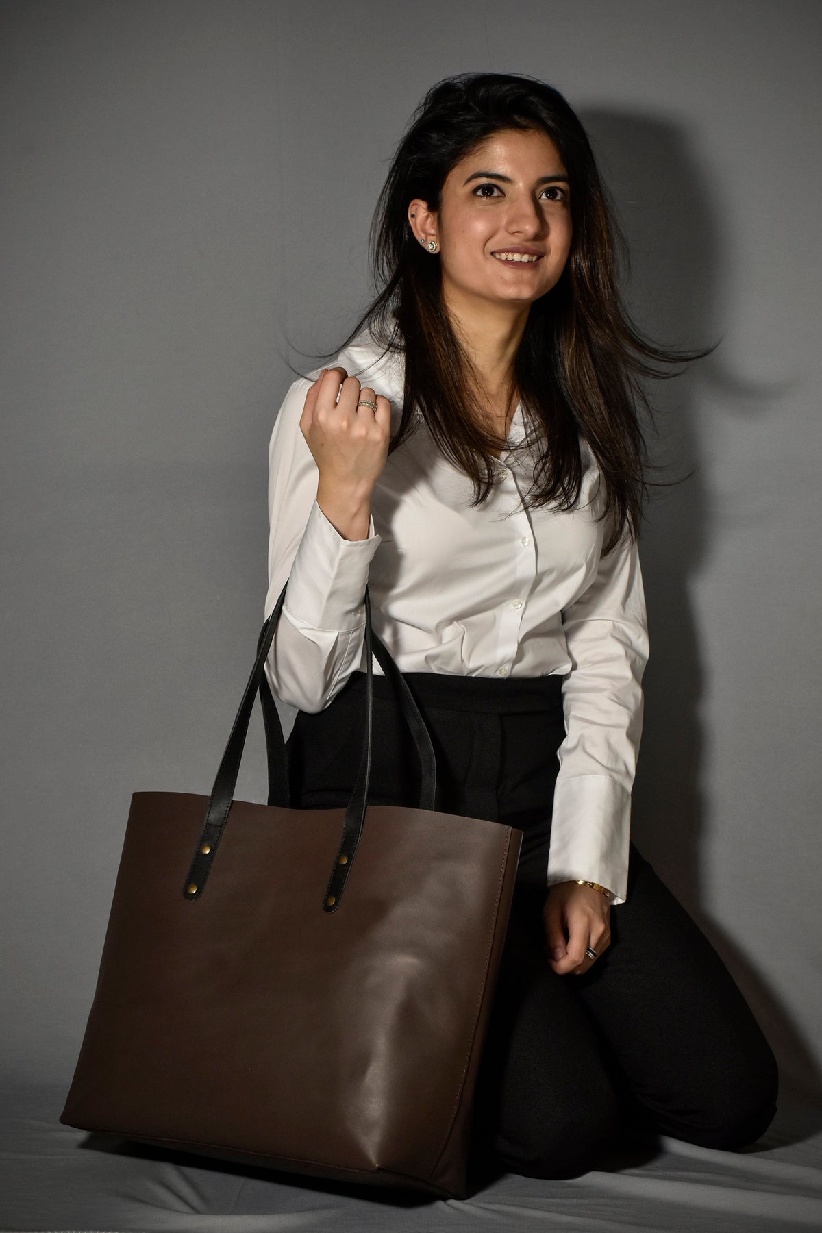 May include: A brown leather tote bag with black handles and gold accents. The bag is large enough to carry a laptop or other essentials.