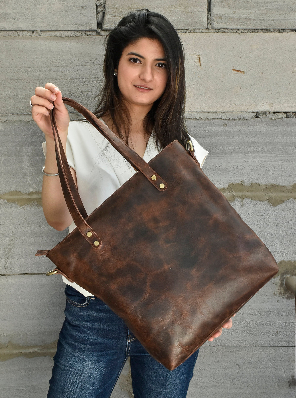 May include: A brown leather tote bag with a zipper closure and two top handles. The bag has a distressed look and is made of high-quality leather.