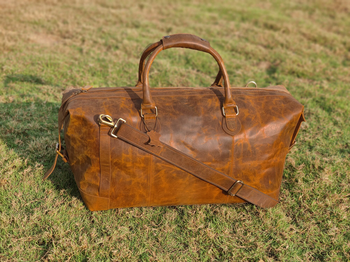 May include: A brown leather duffel bag with a top handle and a shoulder strap. The bag has a distressed look and is made of high-quality leather.