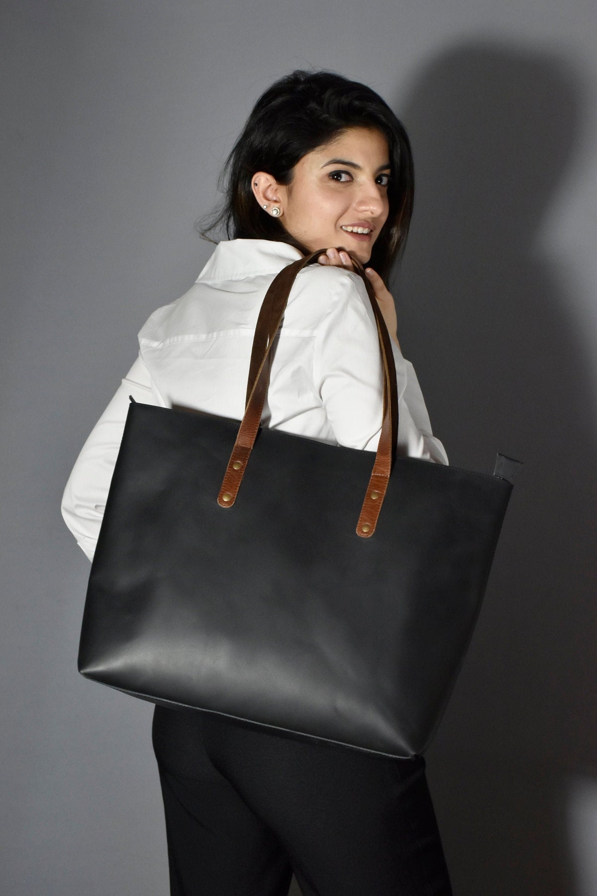 May include: A black leather tote bag with brown leather straps and gold accents. The bag has a spacious interior and is perfect for carrying everyday essentials.