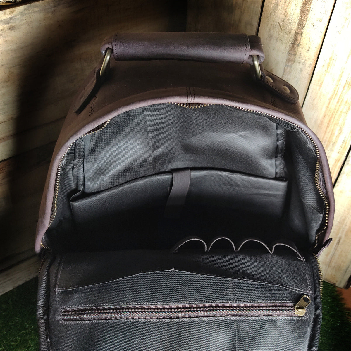 May include: A brown leather backpack with multiple pockets and a zippered compartment. The backpack is open and the interior is visible.