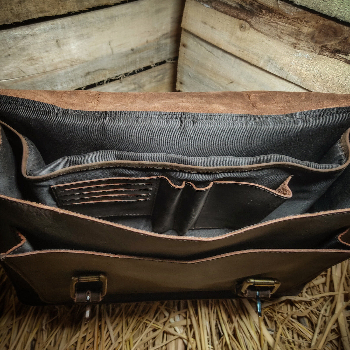 May include: Open view of a brown leather briefcase with multiple interior compartments. The bag has a flap closure with metal clasps and a dark gray interior lining. The leather has a distressed appearance, and the bag appears to be new.