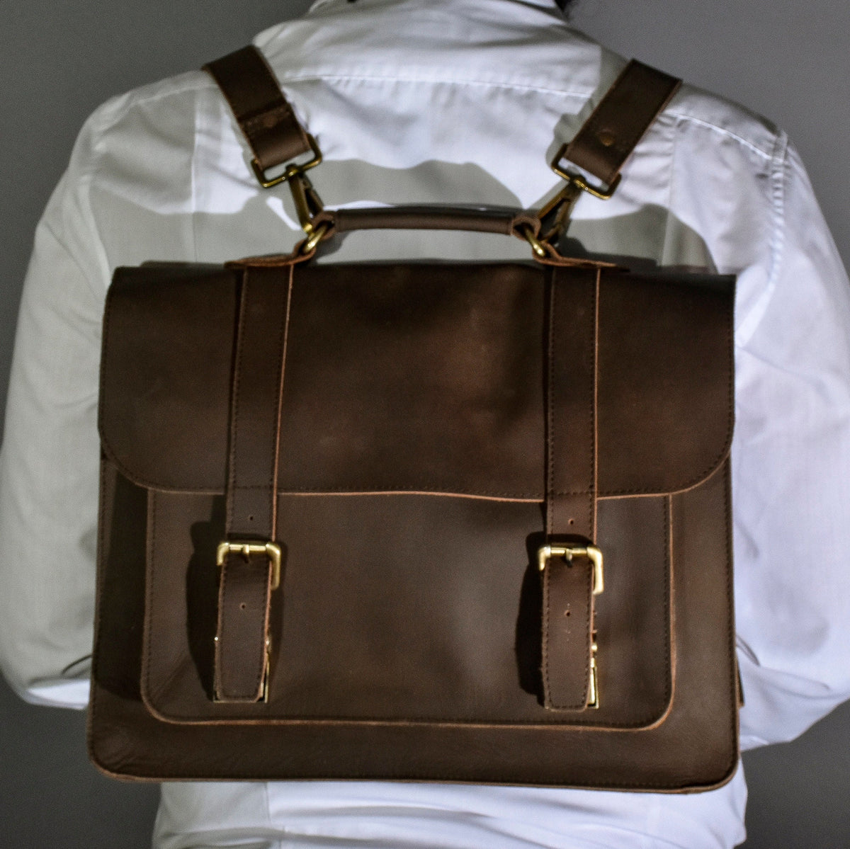 May include: A brown leather satchel backpack with gold buckles and straps. The bag has a flap closure and a top handle.