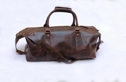 May include: A brown leather duffel bag with a top handle and a long adjustable shoulder strap. The bag has brass hardware and a zipper closure.