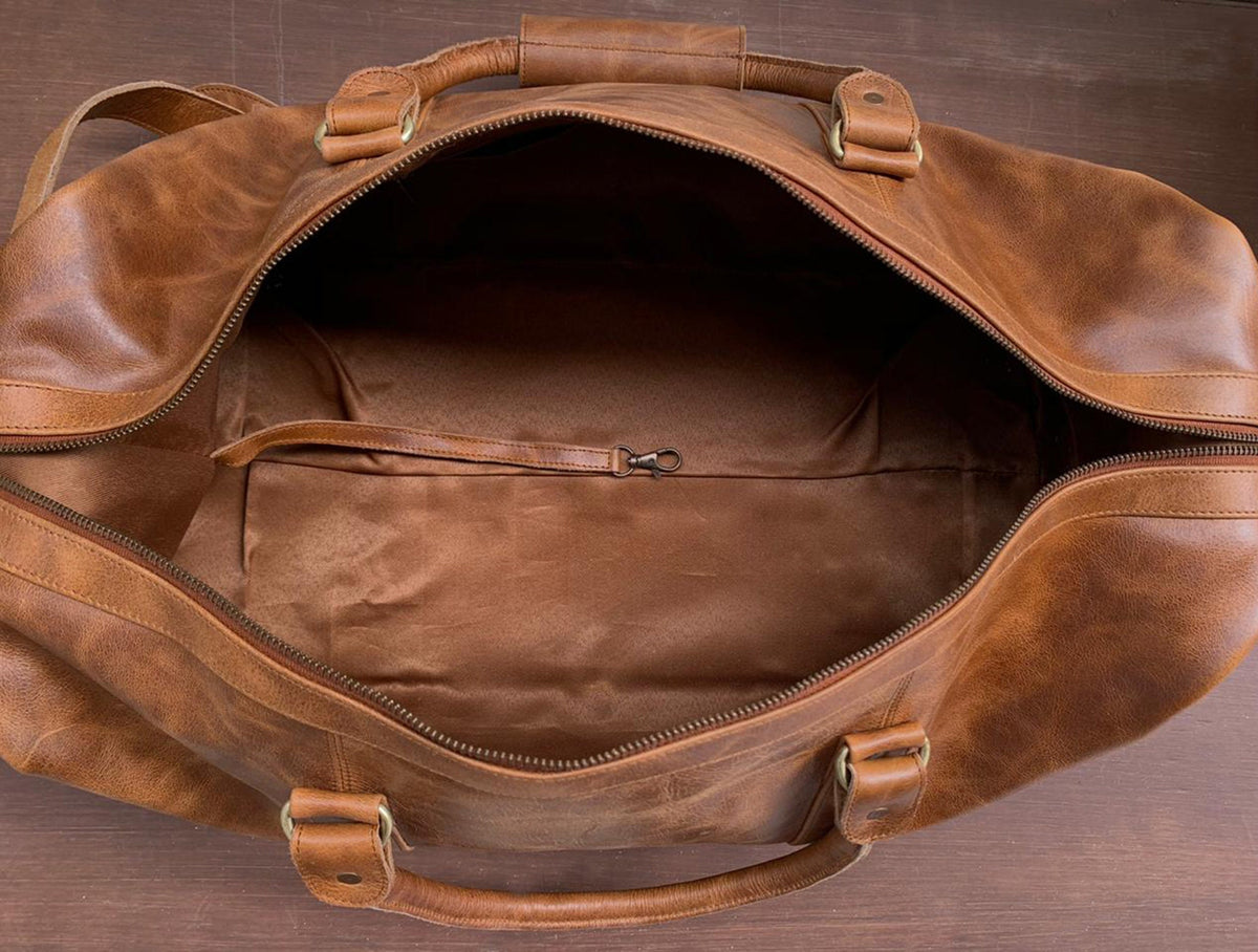 May include: A brown leather duffel bag with a zipper closure and two handles. The bag is open and the inside is lined with a brown fabric.