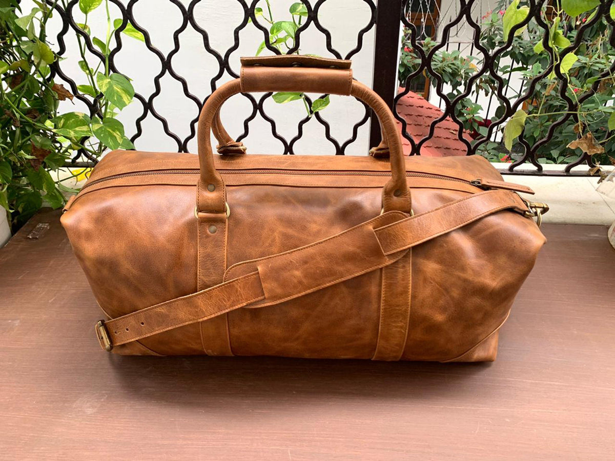 May include: A brown leather duffel bag with a top handle and a shoulder strap. The bag has a zipper closure and brass hardware.
