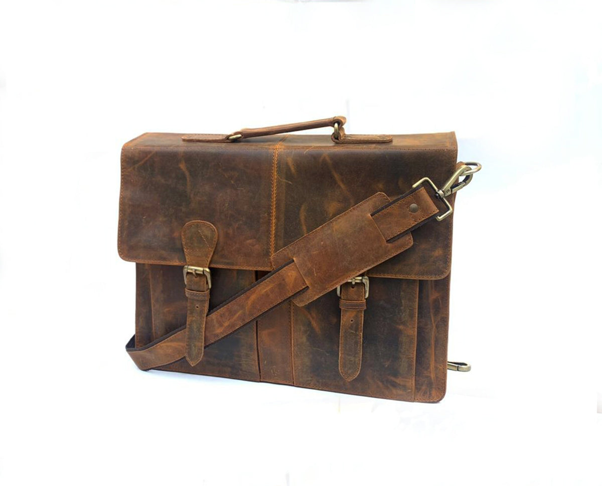May include: A brown leather briefcase with a top handle and adjustable shoulder strap. The bag features two front buckles and a flap closure. The leather has a distressed appearance with visible grain and texture, and the hardware is gold-toned.