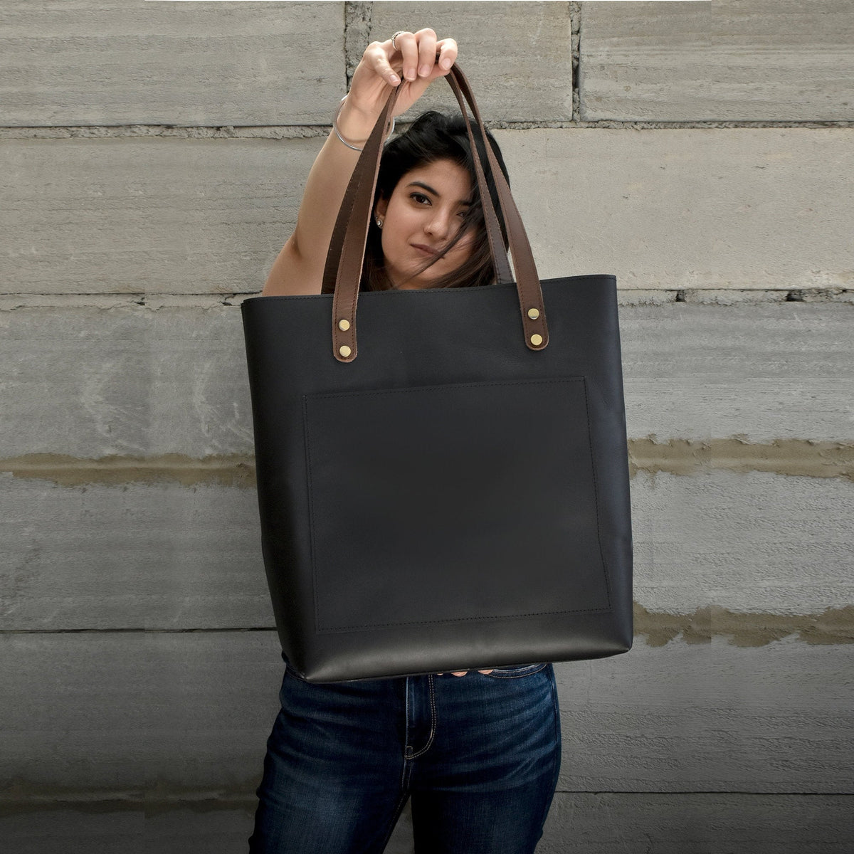 Black leather tote bag comes with contrasting brown handles to elevate the look of the bag. This black leather purse is perfect to fit up to 15 inch laptop with ample of space to carry essentials for an entire day of running errands or to work.