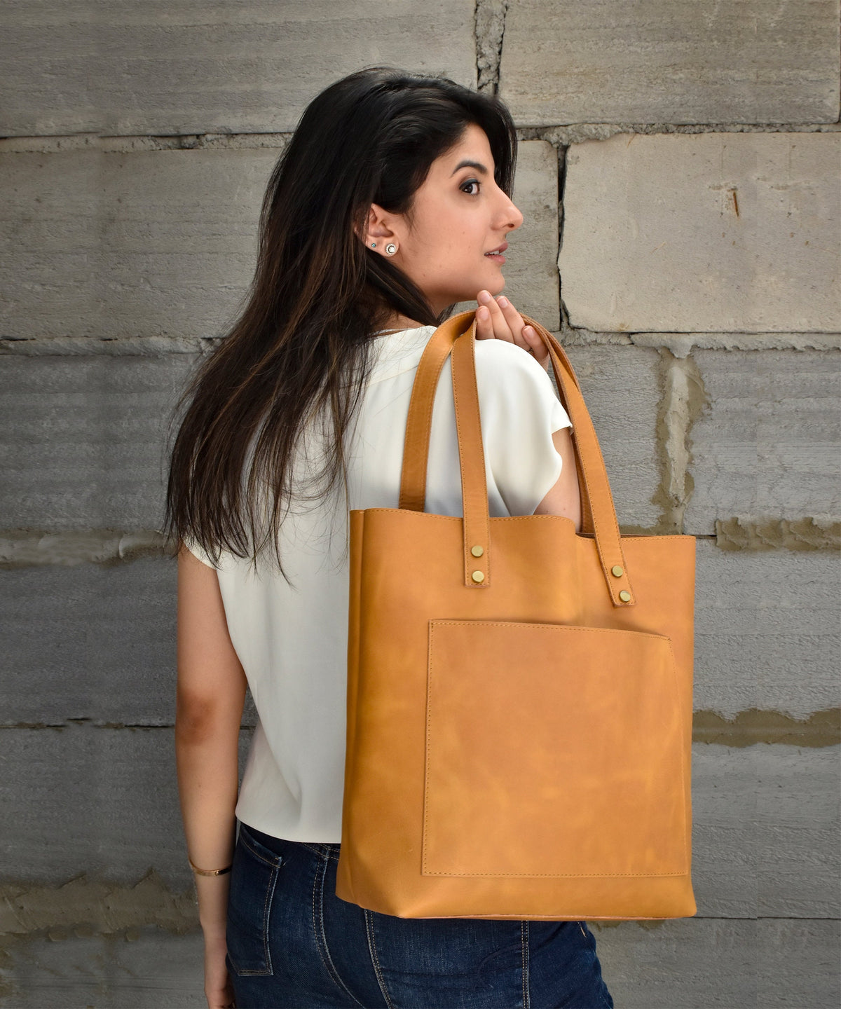 May include: A tan leather tote bag with a front pocket and brass accents. The bag has a top handle and a shoulder strap.