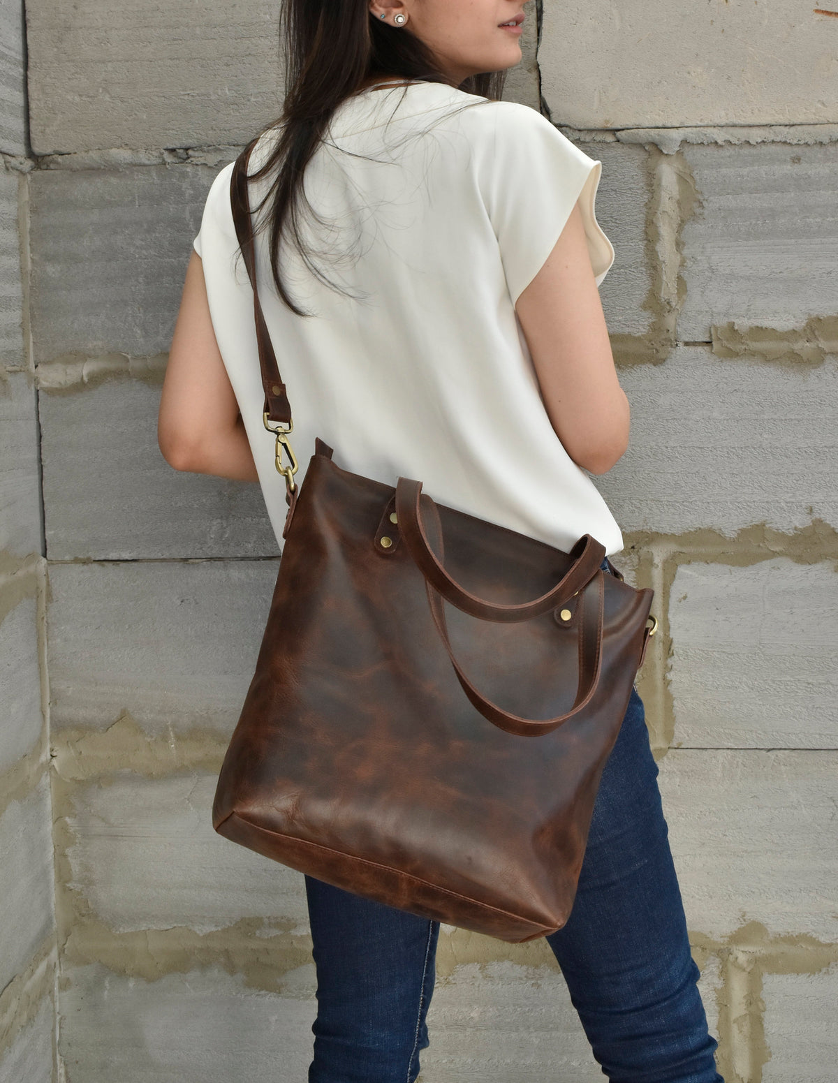 May include: A brown leather tote bag with a long strap. The bag has a top zipper closure and two top handles.