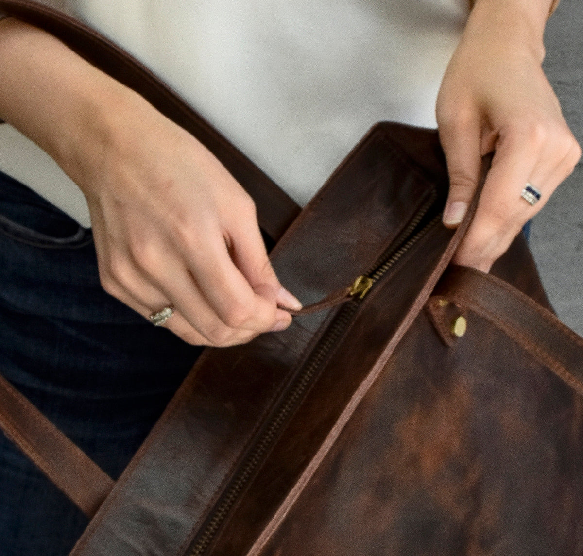 May include: A brown leather tote bag with a zipper closure and a brass buckle. The bag has a distressed look and is made of high-quality leather.