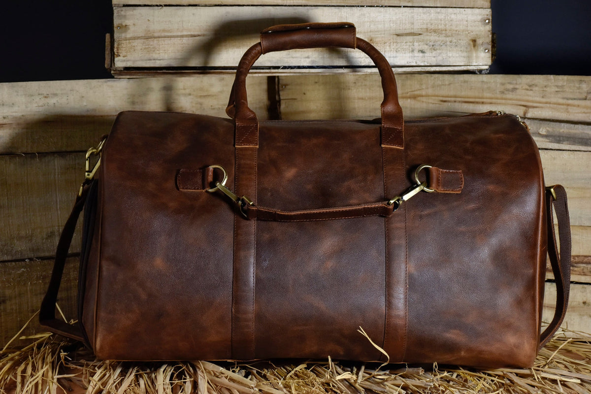 May include: A brown leather duffel bag with a top handle and two shoulder straps. The bag has brass hardware and a distressed leather finish.