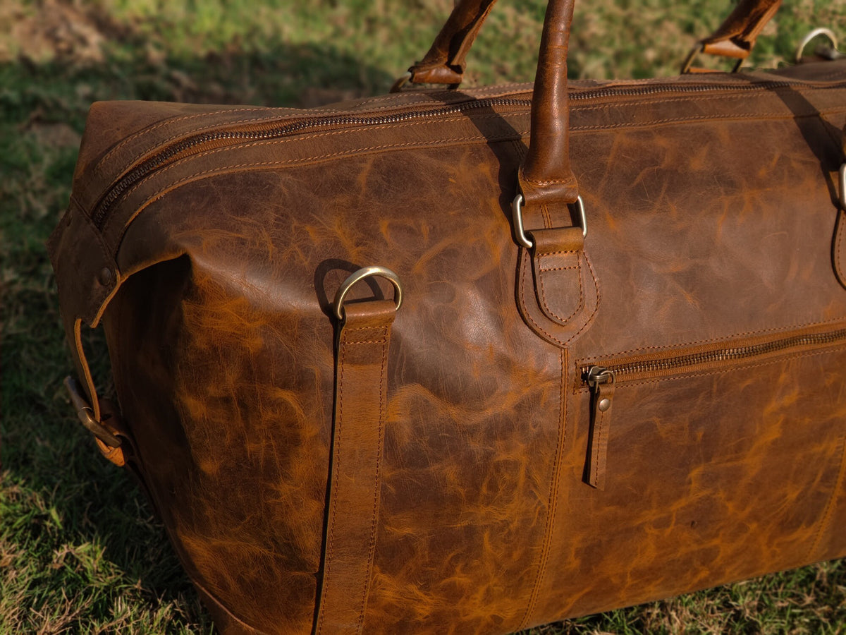May include: A brown leather duffel bag with two top handles and a zippered closure. The bag has a distressed look and is made of high-quality leather.