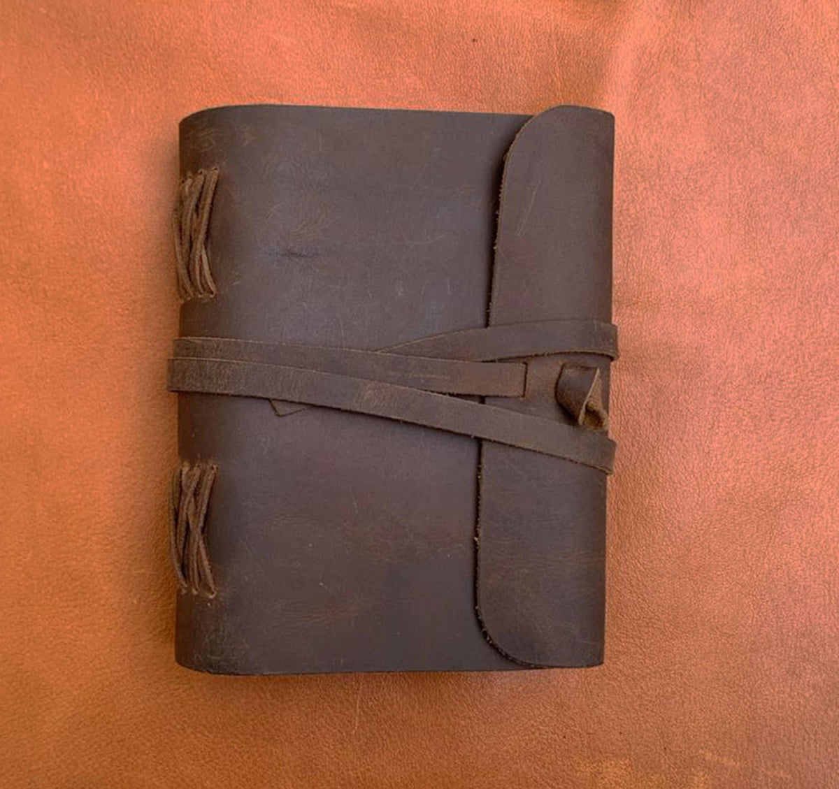 May include: A brown leather journal with a flap closure and a braided leather strap. The journal has a rustic, vintage look.