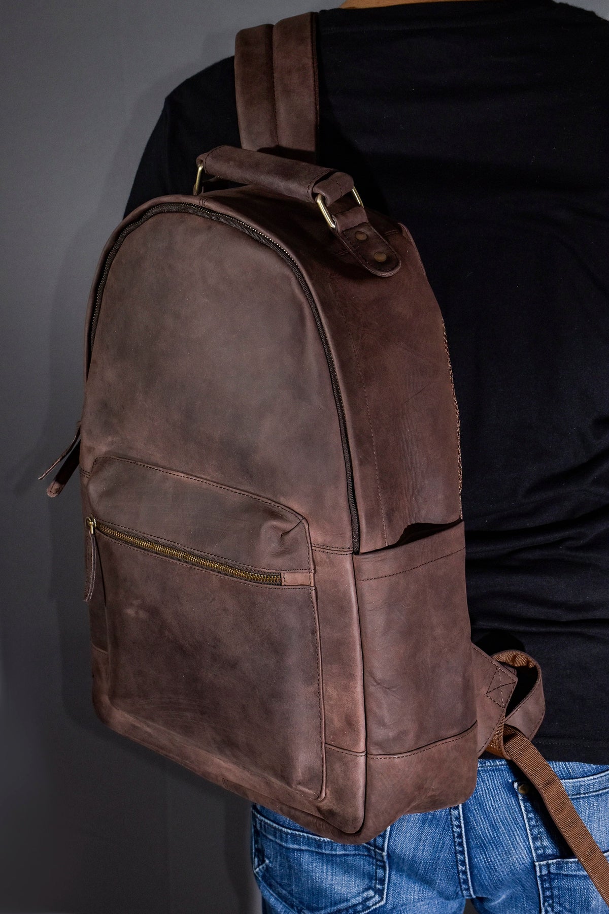 May include: A brown leather backpack with a zippered pocket on the front and adjustable straps.