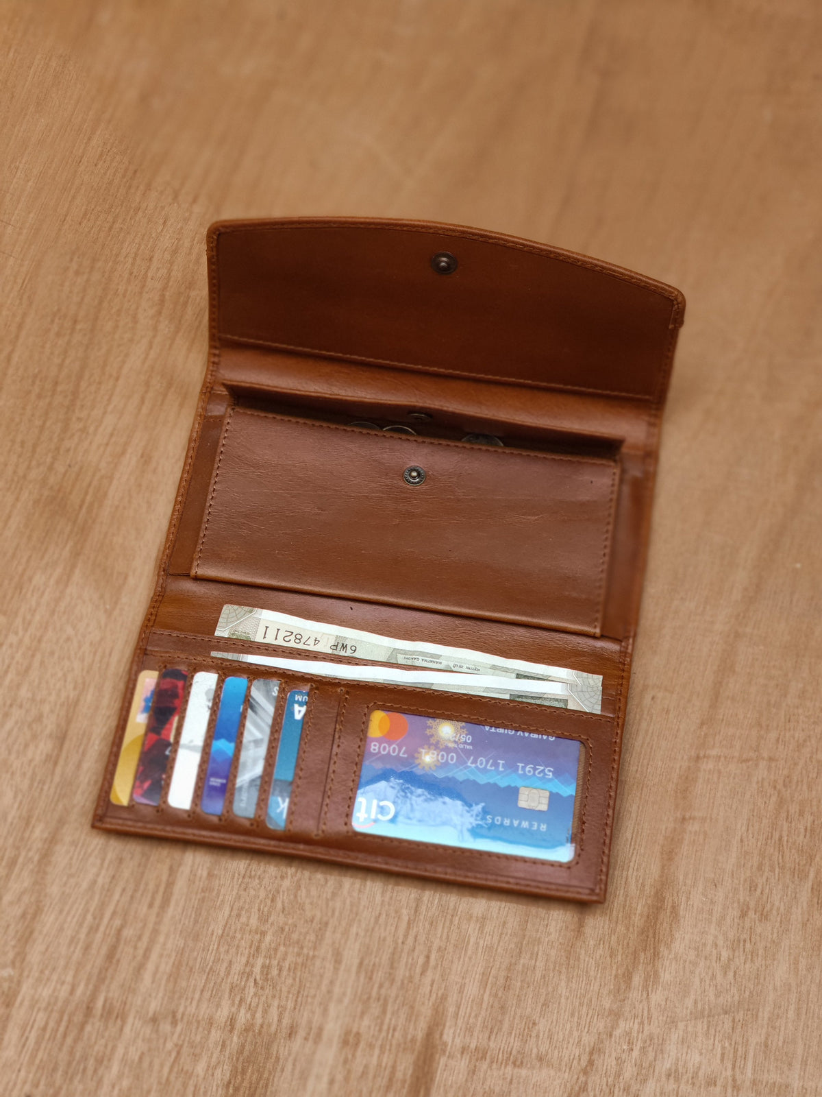 May include: A brown leather wallet with multiple credit cards and cash inside. The wallet is open and the cards are visible. The text on one of the cards reads "Rewards 5261 1707 001 7008 Citi"