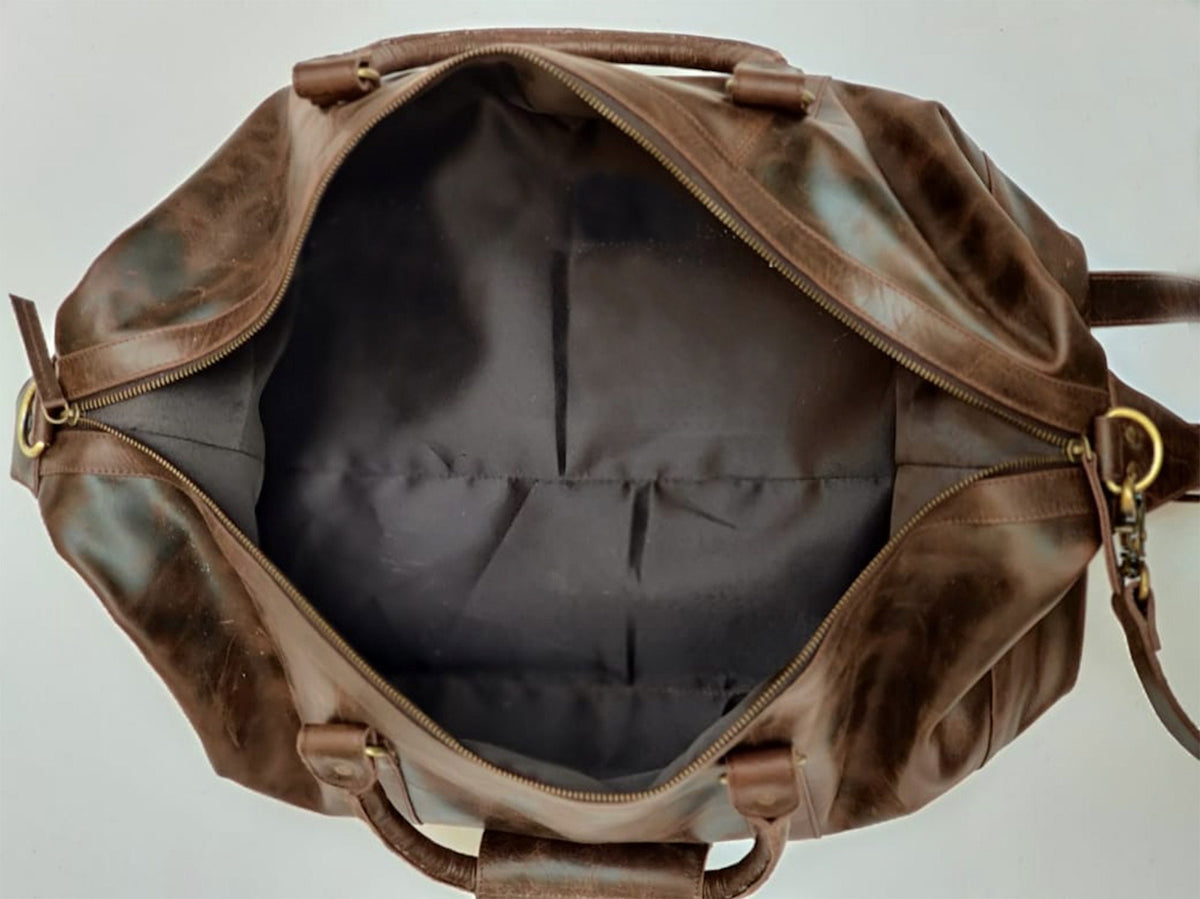 May include: A brown leather duffel bag with a zipper closure and two handles. The bag is open and the inside is lined with a dark fabric.
