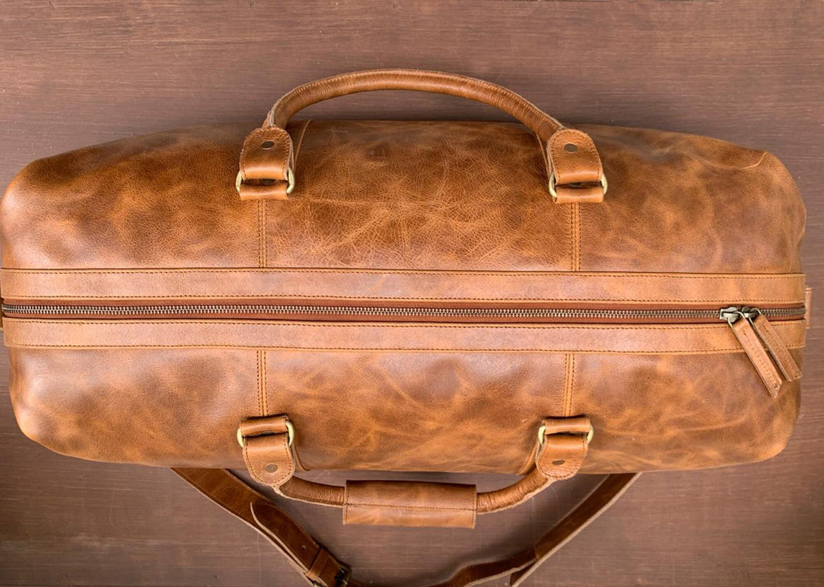 May include: A brown leather duffel bag with a zipper closure and two handles. The bag has a distressed look and is made of high-quality leather.